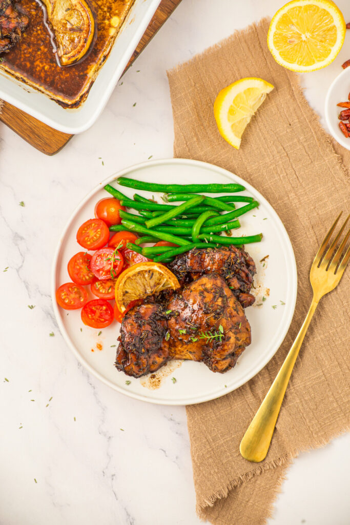 Honey balsamic chicken thighs plated with green beans and tomatoes, garnished with lemon