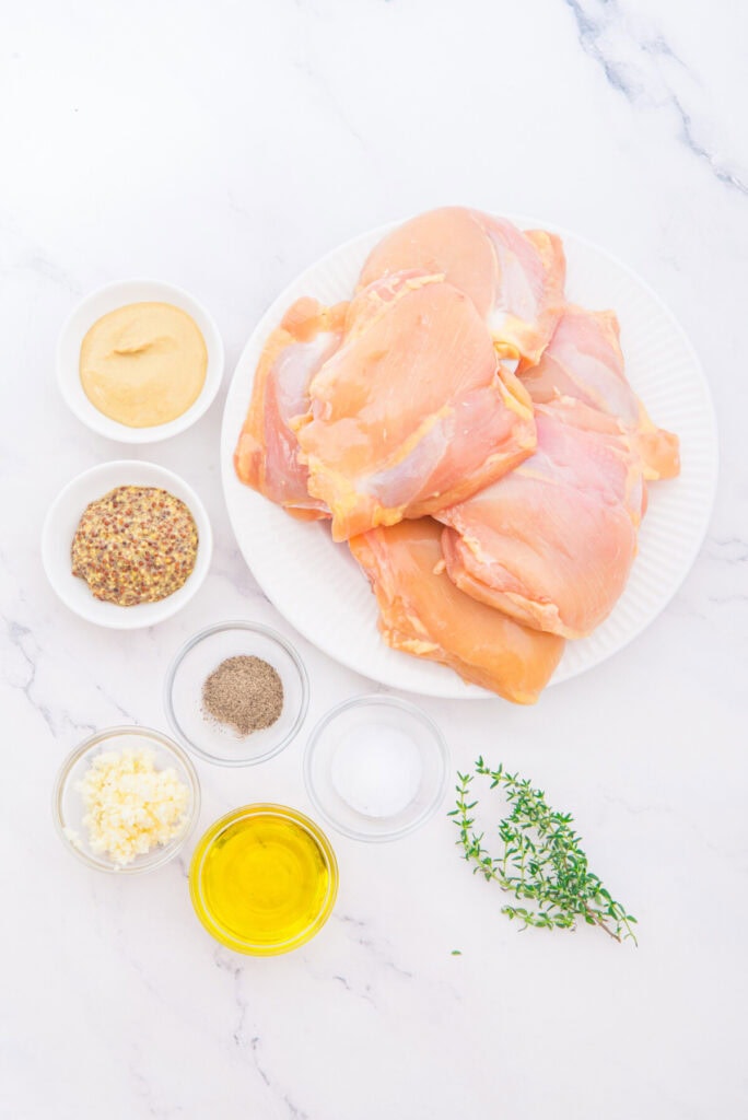 Raw chicken thighs and ingredients for mustard chicken recipe on marble counter