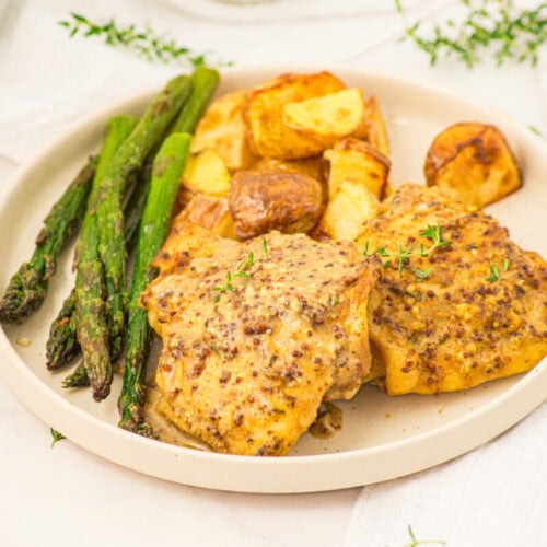 Plated mustard chicken thighs with roasted potatoes and grilled asparagus garnished with thyme