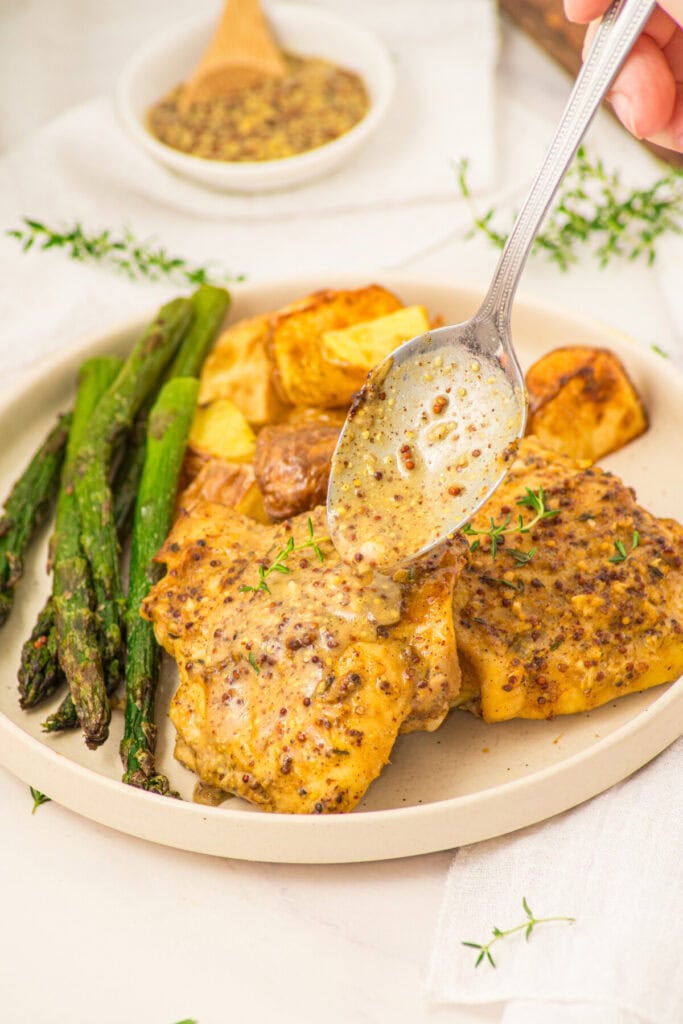 Plated mustard chicken thighs with roasted potatoes and asparagus, drizzled with mustard sauce