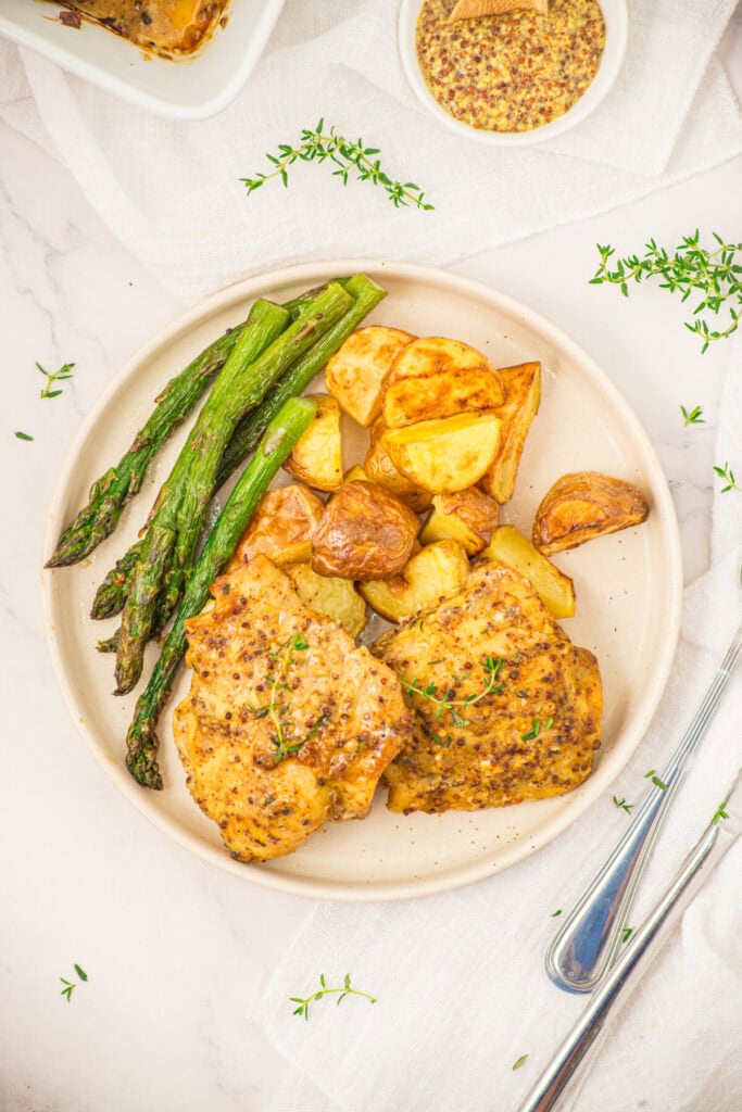 Mustard chicken thighs with roasted asparagus and potatoes, plated and ready to serve