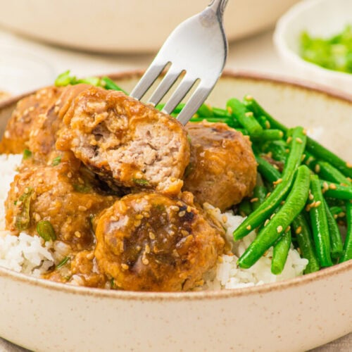 Pork meatballs with soy butter sauce served over rice and green beans in a ceramic bowl