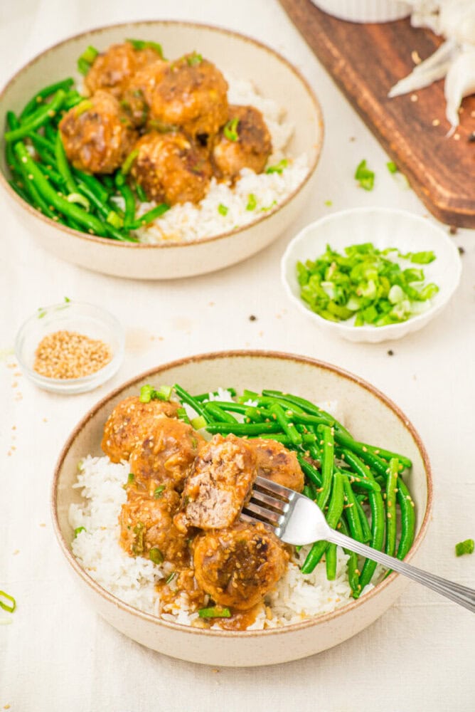 Pork meatballs with soy butter sauce served over rice and green beans, garnished with sesame seeds and green onions