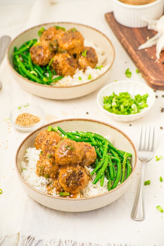 Pork meatballs with soy butter sauce served over rice with green beans, garnished with scallions