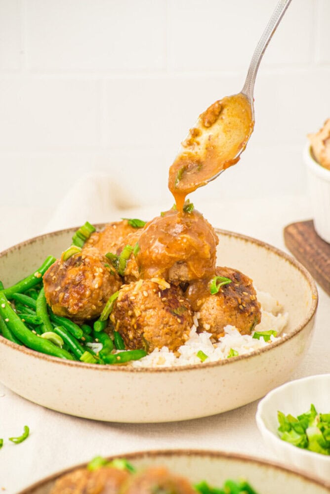 Pork meatballs with soy butter sauce being spooned onto a plate with green beans and rice