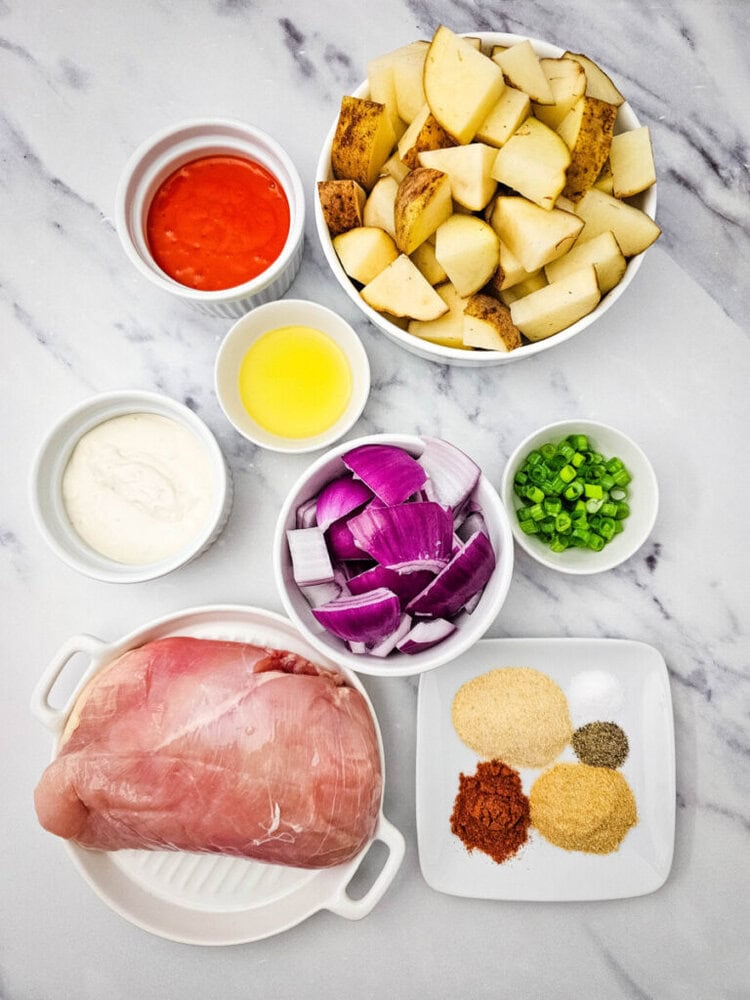 Sheet pan buffalo chicken ingredients overhead view - raw chicken, potatoes, onions, and seasonings on marble