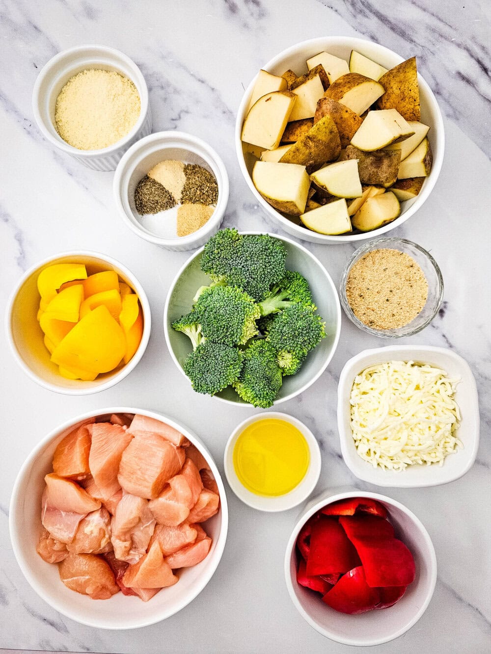 Sheet pan mozzarella chicken ingredients laid out in bowls before cooking - chicken, potatoes, broccoli, peppers, and seasonings