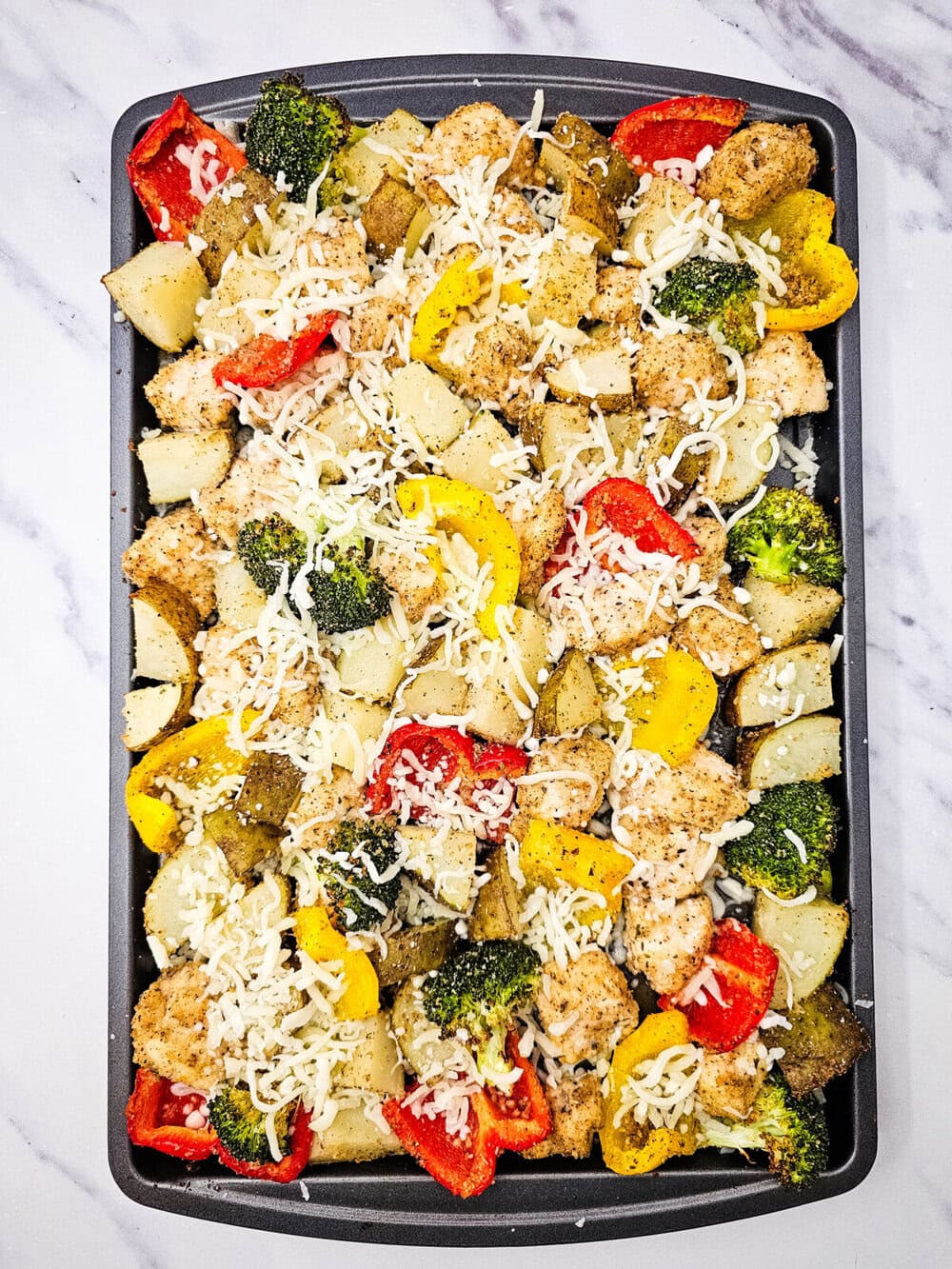 Sheet pan mozzarella chicken with roasted vegetables and melted cheese on dark baking sheet