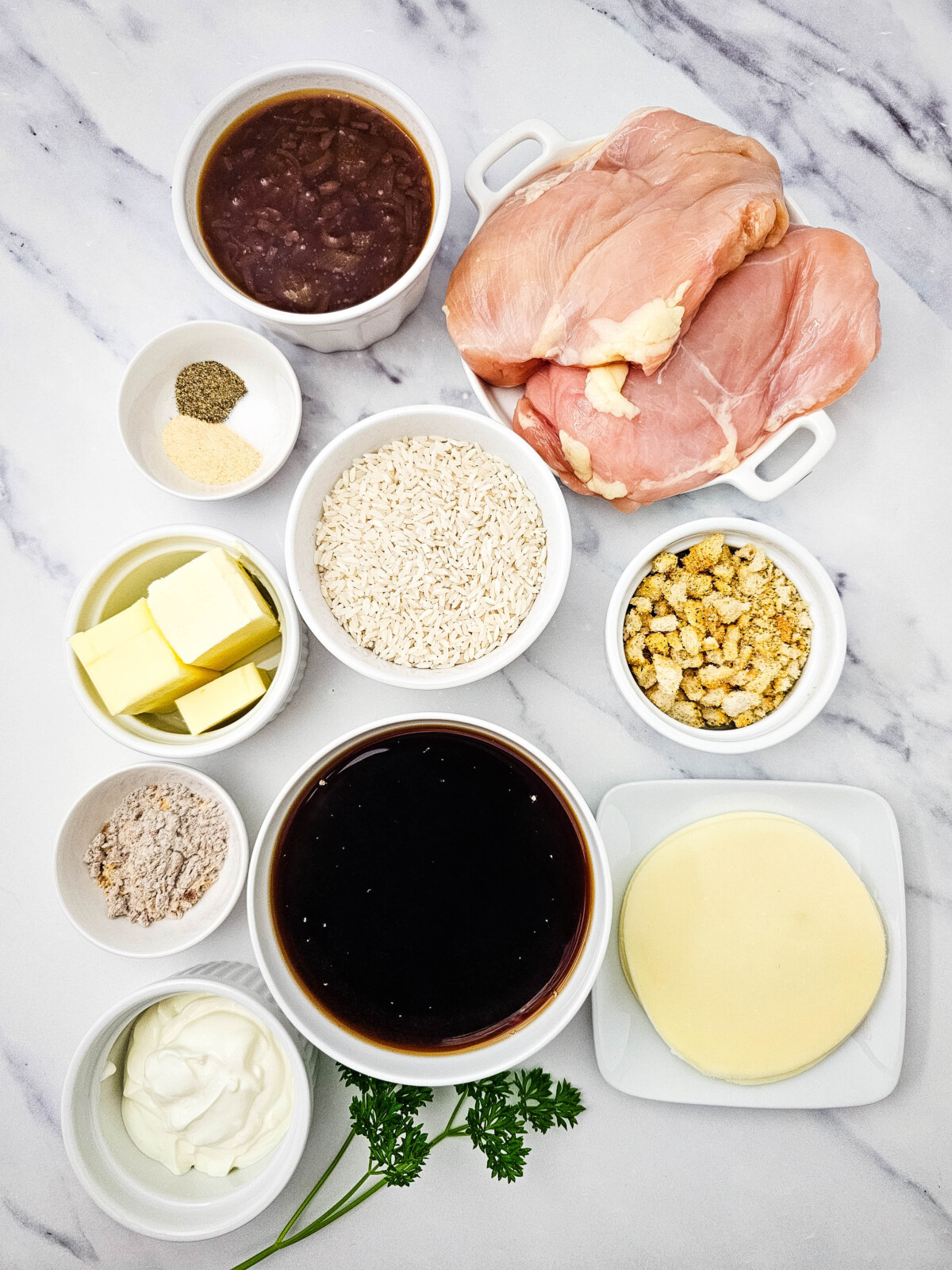 Prepped ingredients for French Onion Chicken and Rice recipe including chicken breast, rice, butter, cream, broth, and seasonings in white bowls