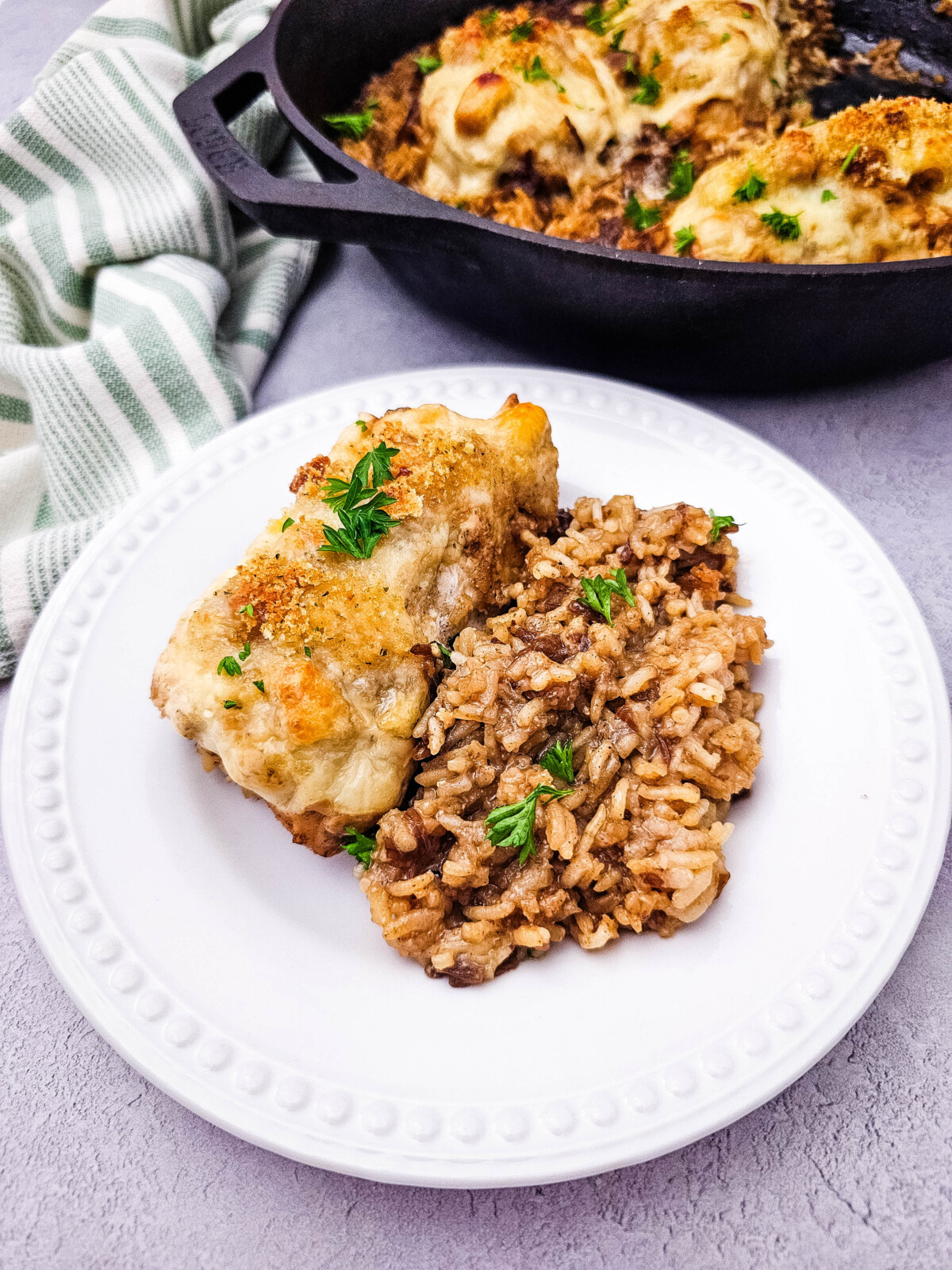 Skillet French onion chicken and rice plated with golden chicken thigh and caramelized onion rice garnished with parsley
