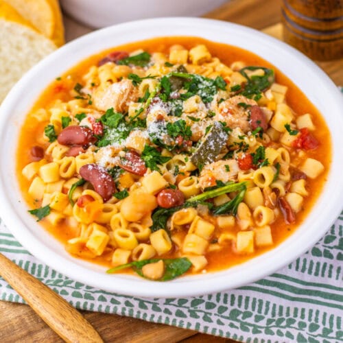 Slow cooker chicken minestrone soup in white bowl with small pasta, beans, and fresh herbs garnish