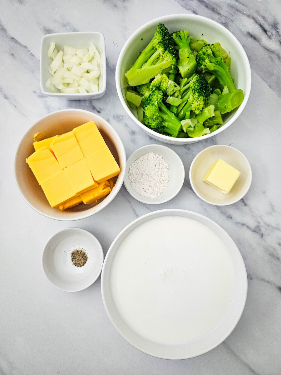 Velveeta cheese broccoli soup ingredients prepped and arranged in bowls including broccoli, Velveeta cheese, onions, butter, cream, flour and spices