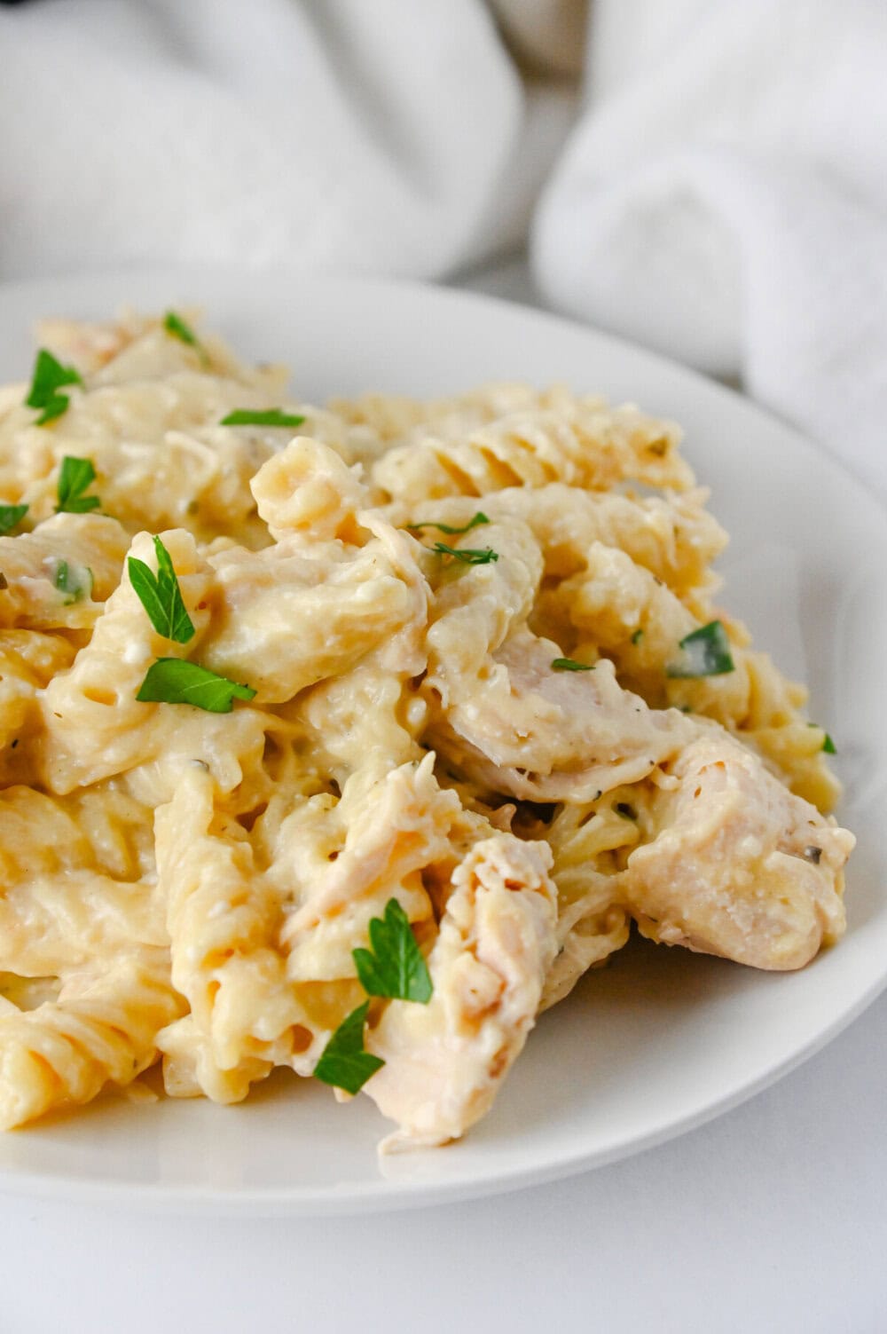 Crockpot ranch chicken pasta with rotini noodles, tender chicken pieces, and fresh parsley garnish on a white plate