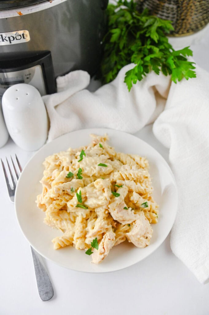 Crockpot ranch chicken pasta with bow-tie noodles and fresh parsley garnish on white plate