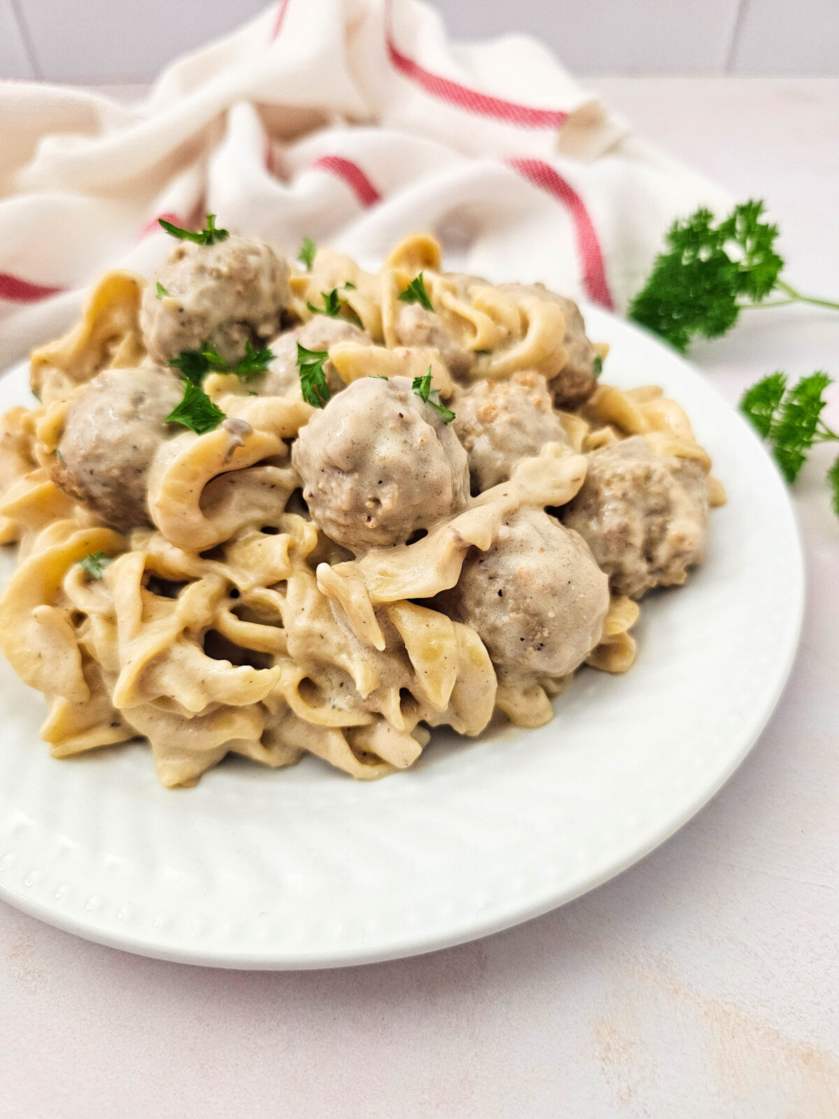 Crockpot Swedish meatballs served over egg noodles with creamy sauce and fresh parsley garnish