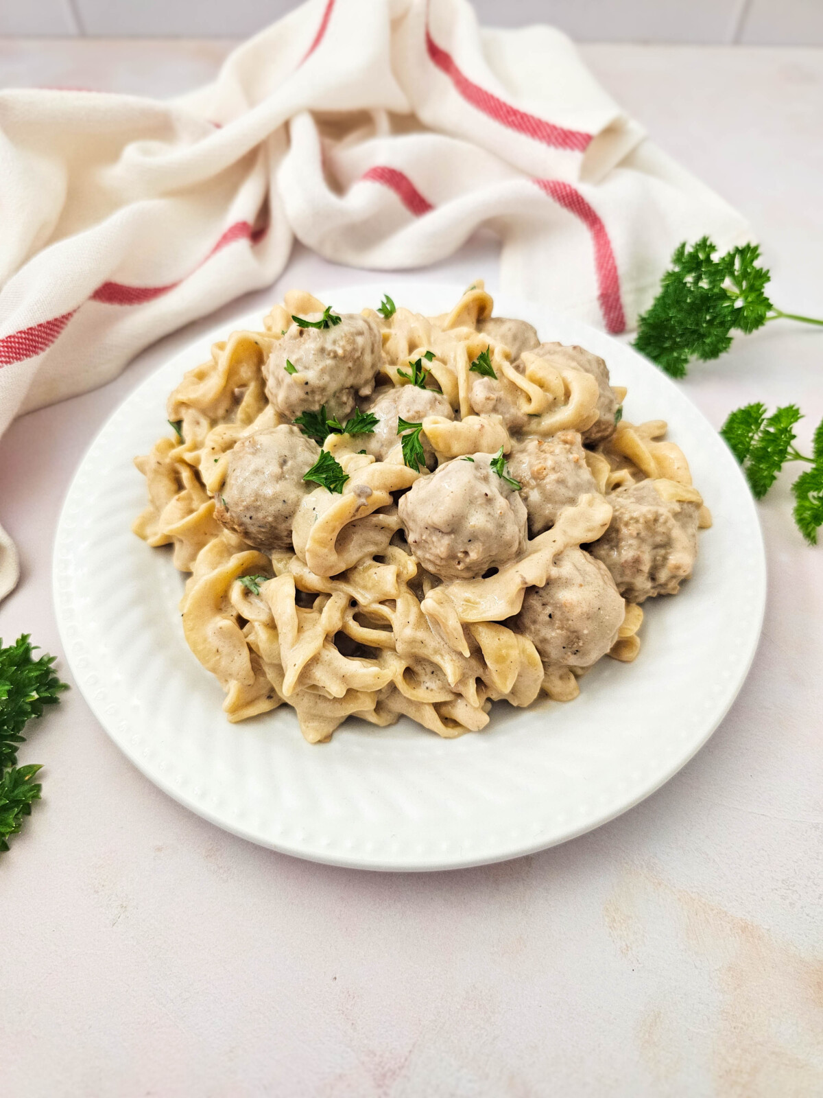 Crockpot Swedish meatballs with egg noodles in creamy sauce garnished with parsley on white plate