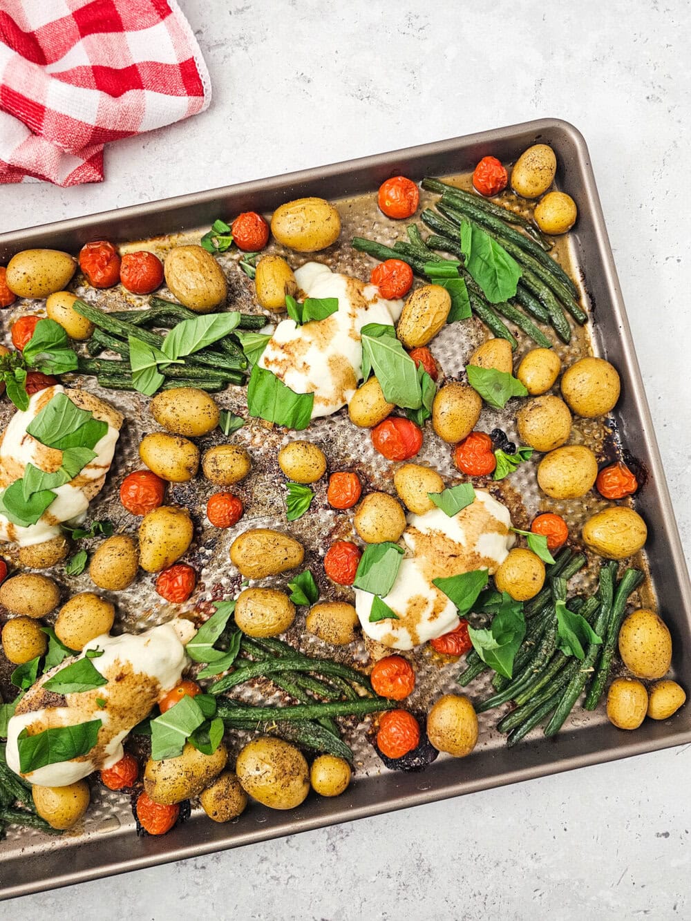 Sheet pan chicken caprese with melted mozzarella, roasted potatoes, green beans, tomatoes and basil garnish