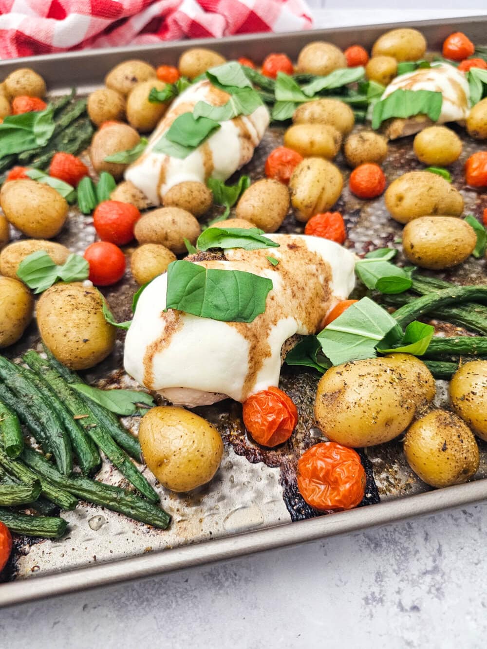 Sheet pan chicken caprese with mozzarella-topped chicken, roasted potatoes, green beans, and tomatoes