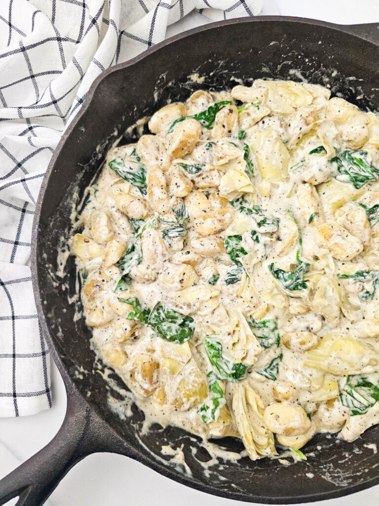 Spinach artichoke gnocchi cooking in cast iron skillet with creamy sauce and fresh greens