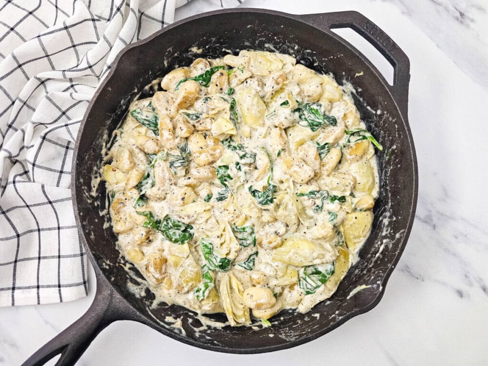 Skillet Spinach Artichoke Gnocchi cooking in cast iron pan with creamy sauce and fresh spinach garnish