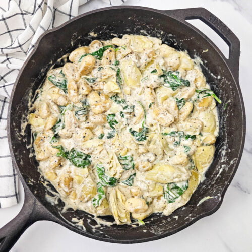 Skillet Spinach Artichoke Gnocchi cooking in cast iron pan with creamy sauce and fresh spinach garnish