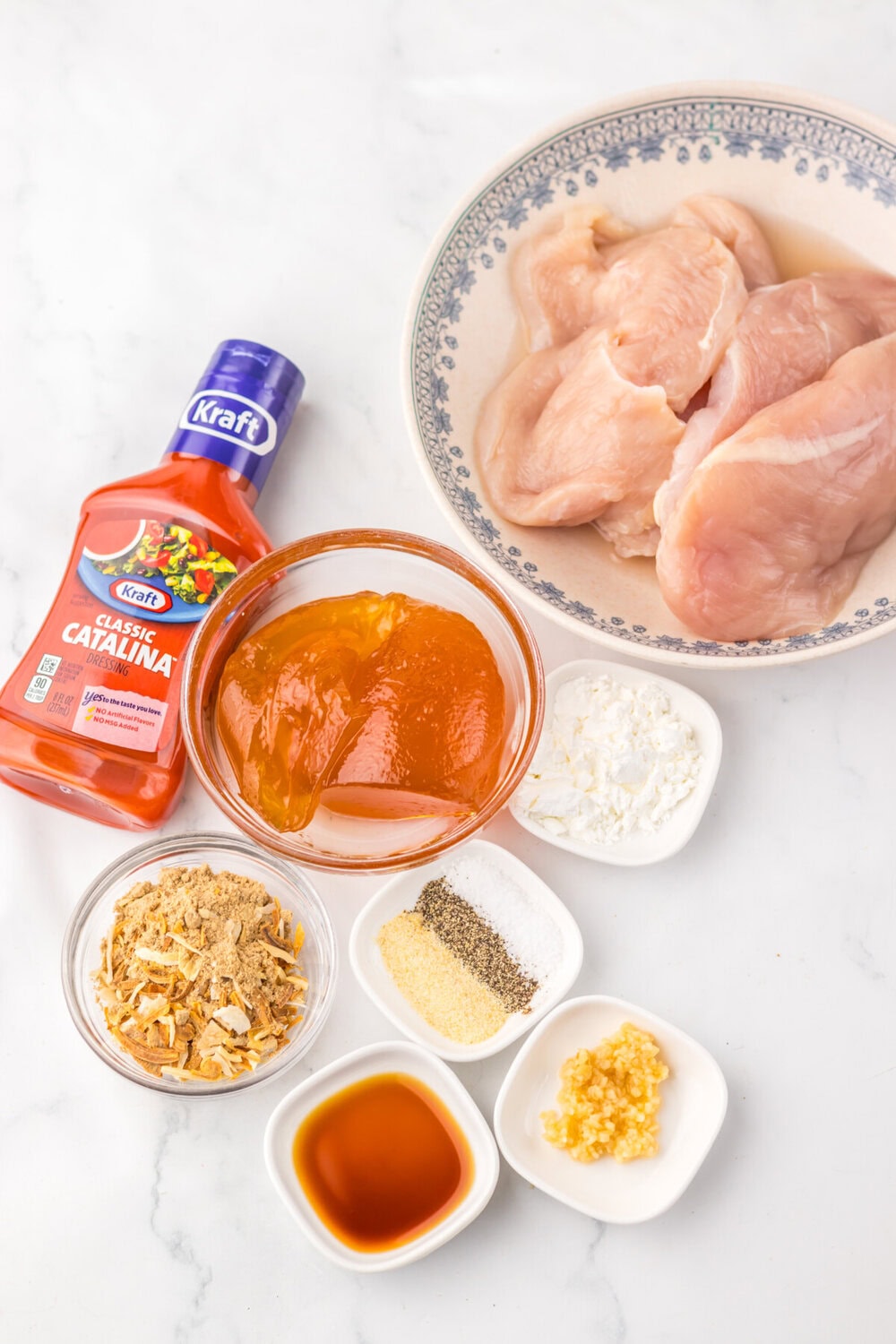 Slow cooker Catalina chicken ingredients laid out including raw chicken, Kraft Catalina dressing, fried onions, garlic, cornstarch and seasonings