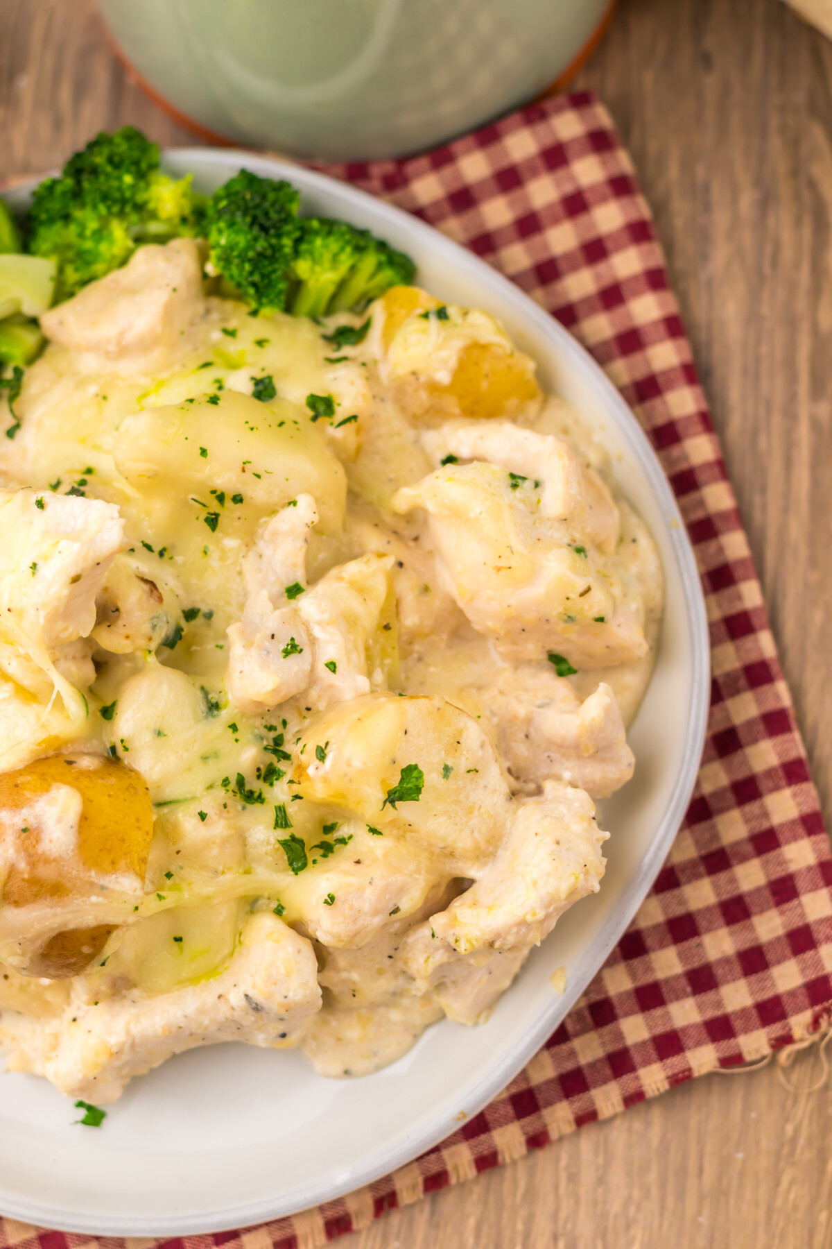 Slow cooker cheesy caesar chicken and potatoes plated with broccoli garnished with parsley