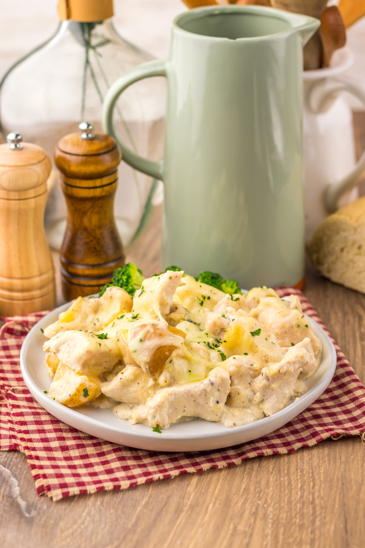Slow cooker cheesy Caesar chicken and potatoes served on white plate with fresh herbs and rustic kitchen styling