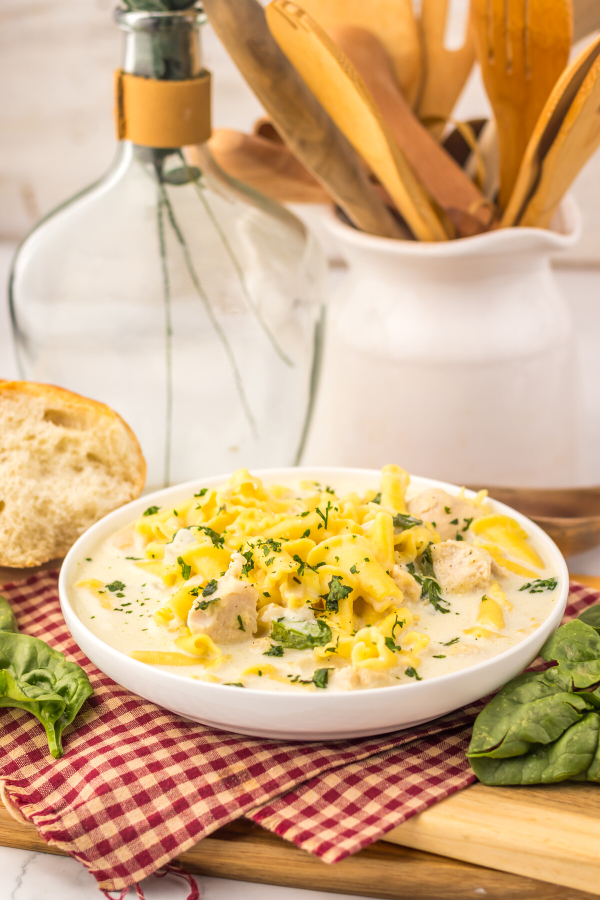 Slow cooker chicken alfredo soup plated in white bowl with noodles, chicken, and fresh herbs garnish