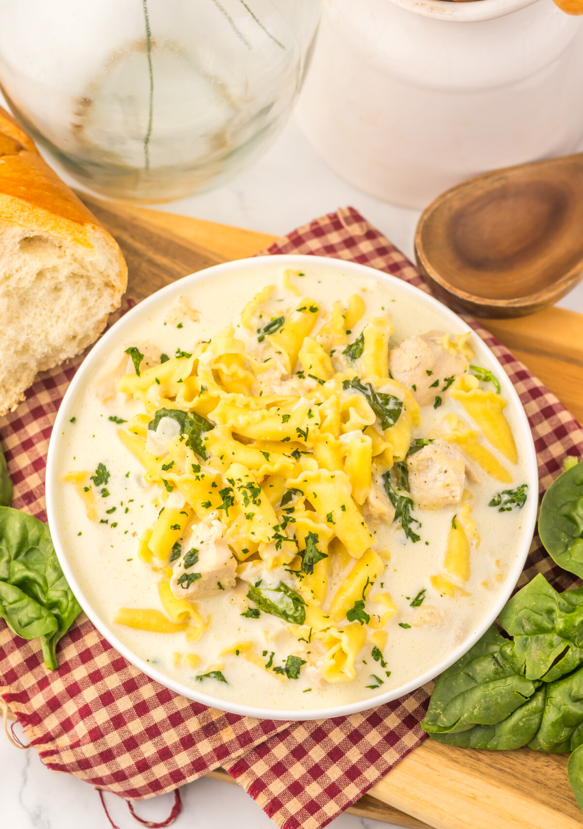 Slow cooker chicken Alfredo soup with penne pasta, chicken, and fresh parsley garnish served in white bowl