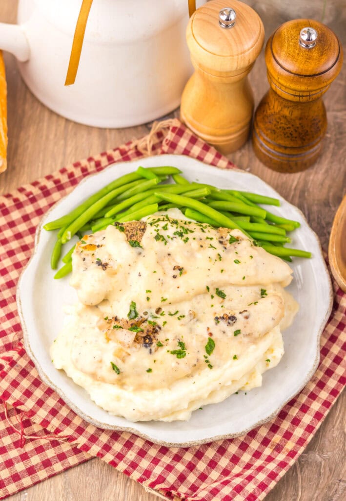 Slow cooker chicken au poivre plated with mashed potatoes and green beans, garnished with cracked black pepper and fresh herbs
