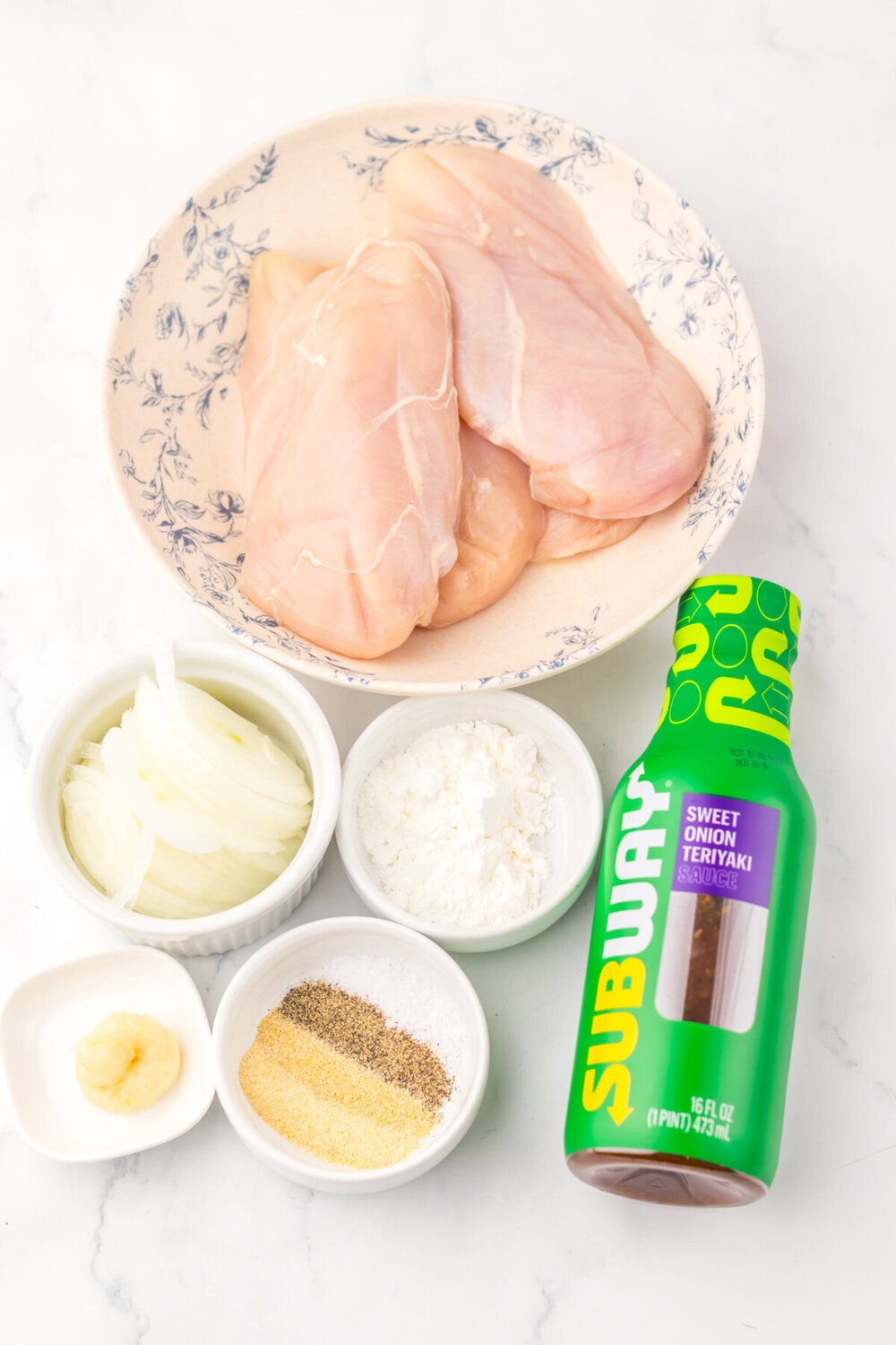 Slow cooker teriyaki chicken ingredients: raw chicken breasts, mayo, cornstarch, garlic, seasonings, and Subway teriyaki sauce on white marble