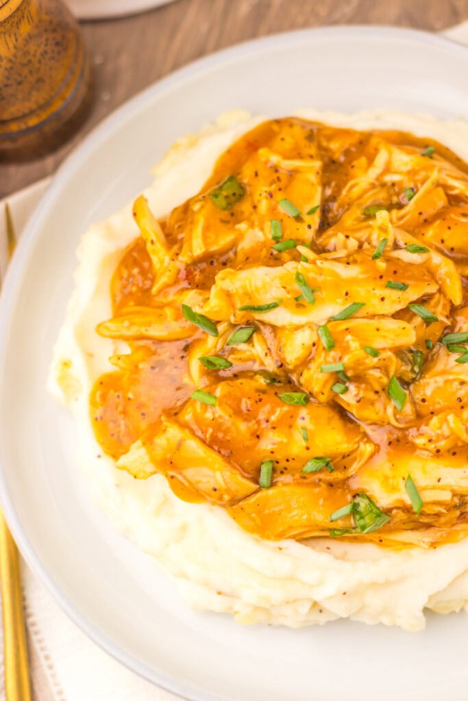 Slow cooker teriyaki chicken with glossy golden sauce served over mashed potatoes, garnished with sliced green onions