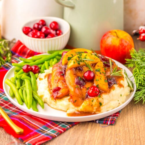 Slow cooker cranberry apple chicken plated with mashed potatoes and green beans, garnished with rosemary and red currants