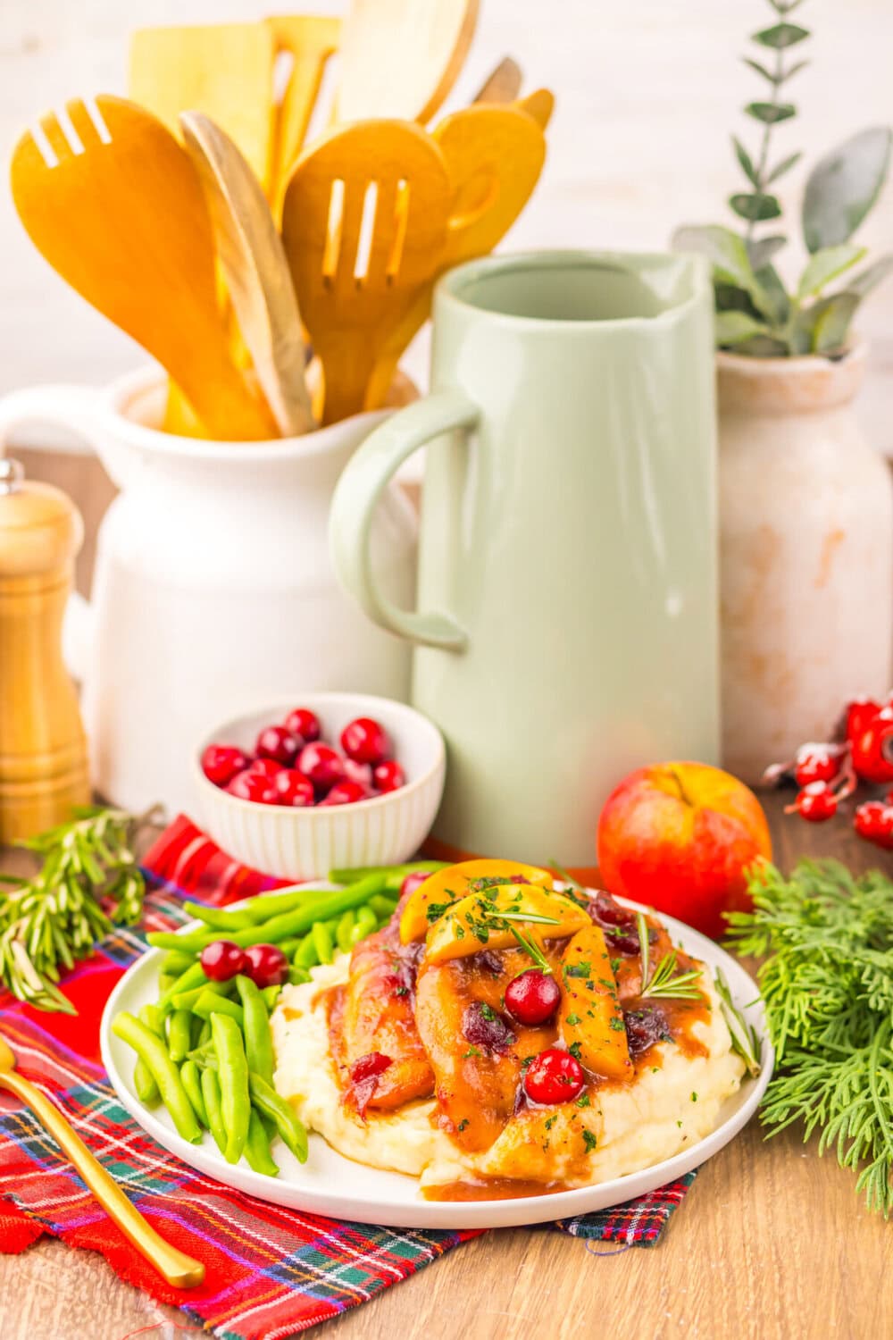Slow cooker cranberry apple chicken served on white plate with mashed potatoes and green beans, garnished with rosemary and cranberries