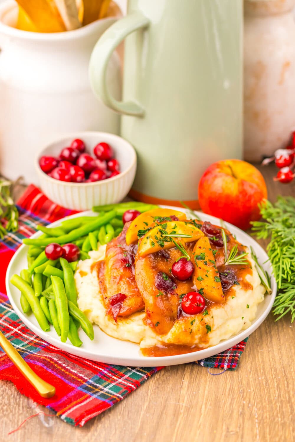 Slow cooker cranberry apple chicken served over mashed potatoes with green beans, garnished with fresh rosemary and cranberries