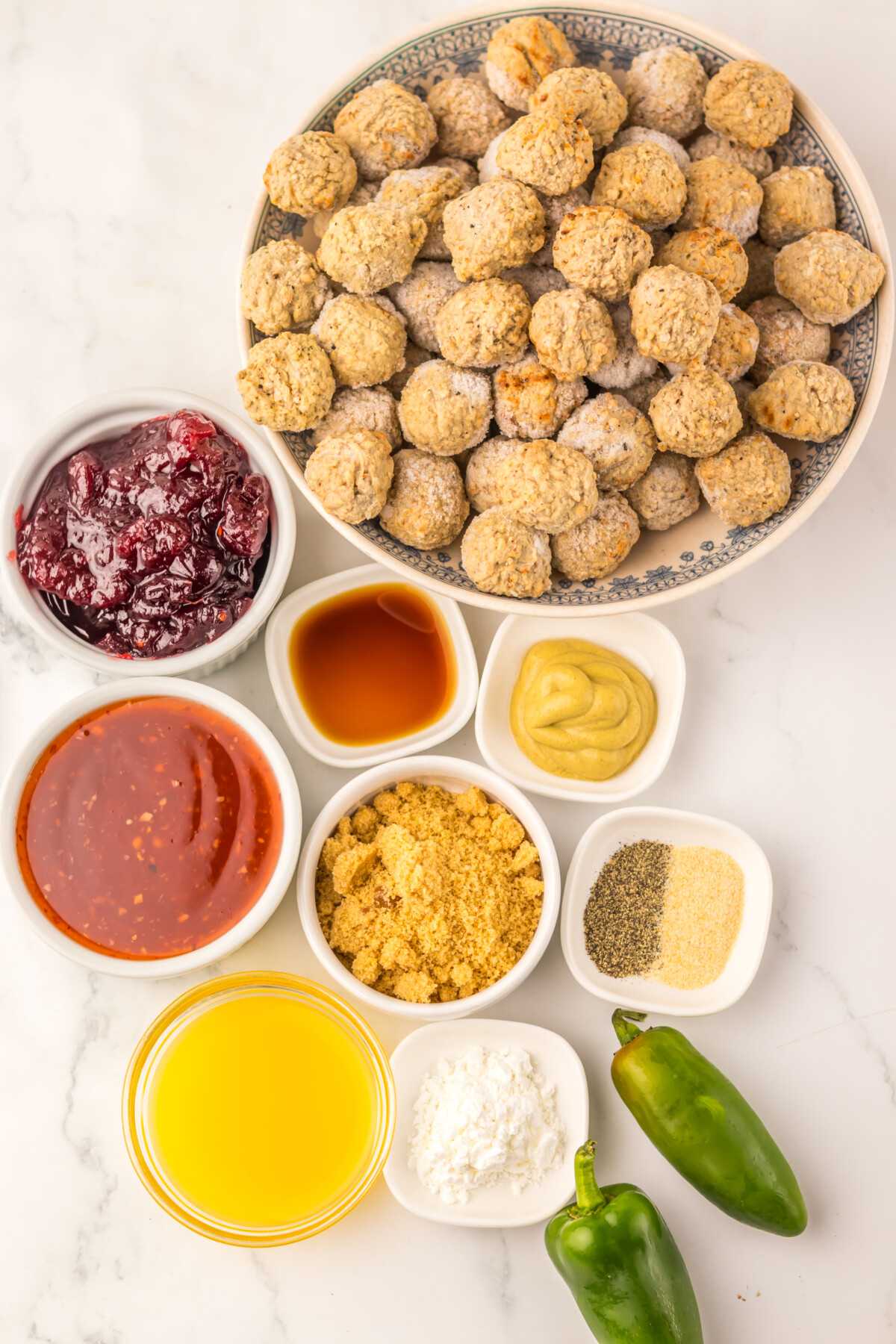 Slow cooker cranberry jalapeño meatballs ingredients laid out overhead including cooked meatballs, cranberry sauce, mustard, spices, oil, and fresh jalapeños