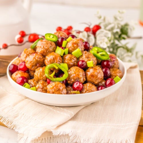 Slow cooker cranberry jalapeño meatballs in white bowl with jalapeño slices and cranberries garnish