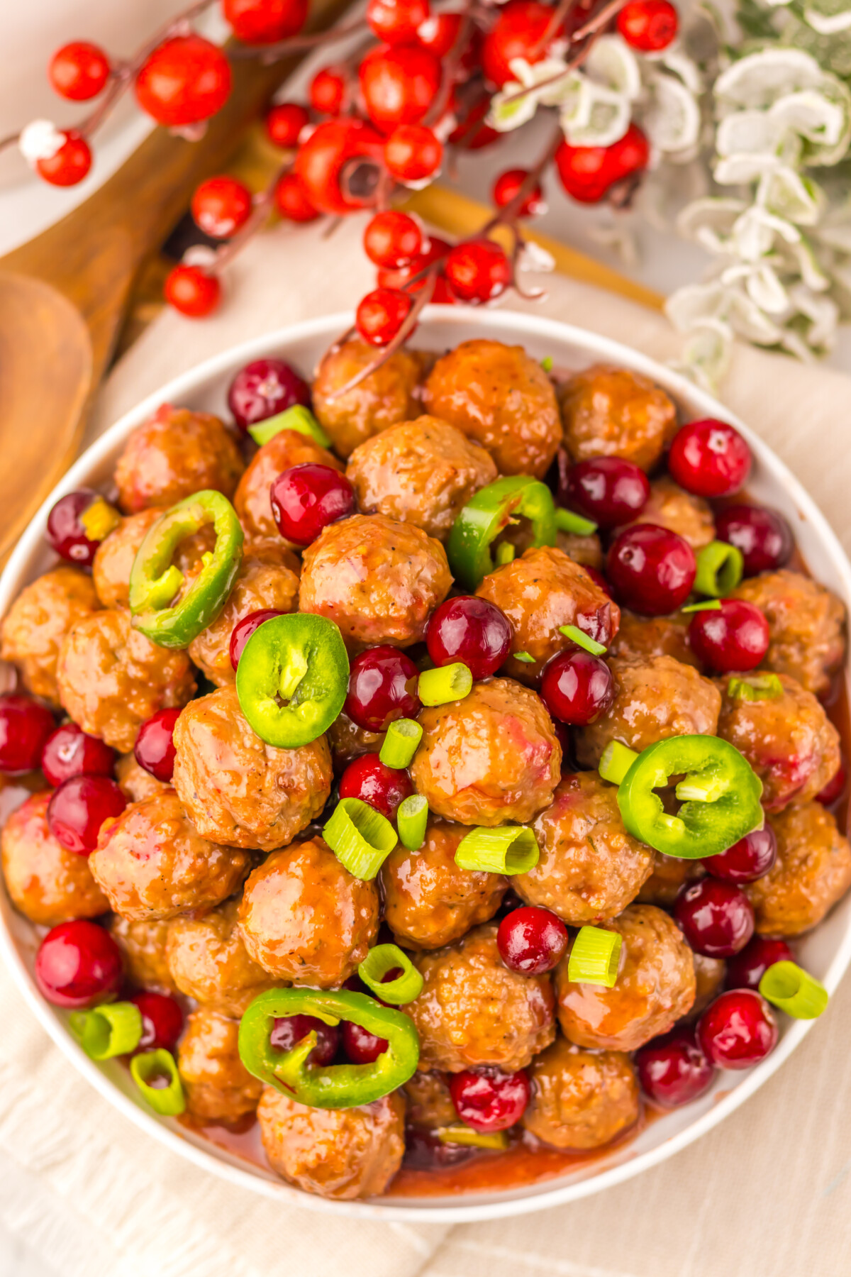 Slow cooker cranberry jalapeño meatballs garnished with fresh green jalapeño slices and red cranberries in a white serving bowl