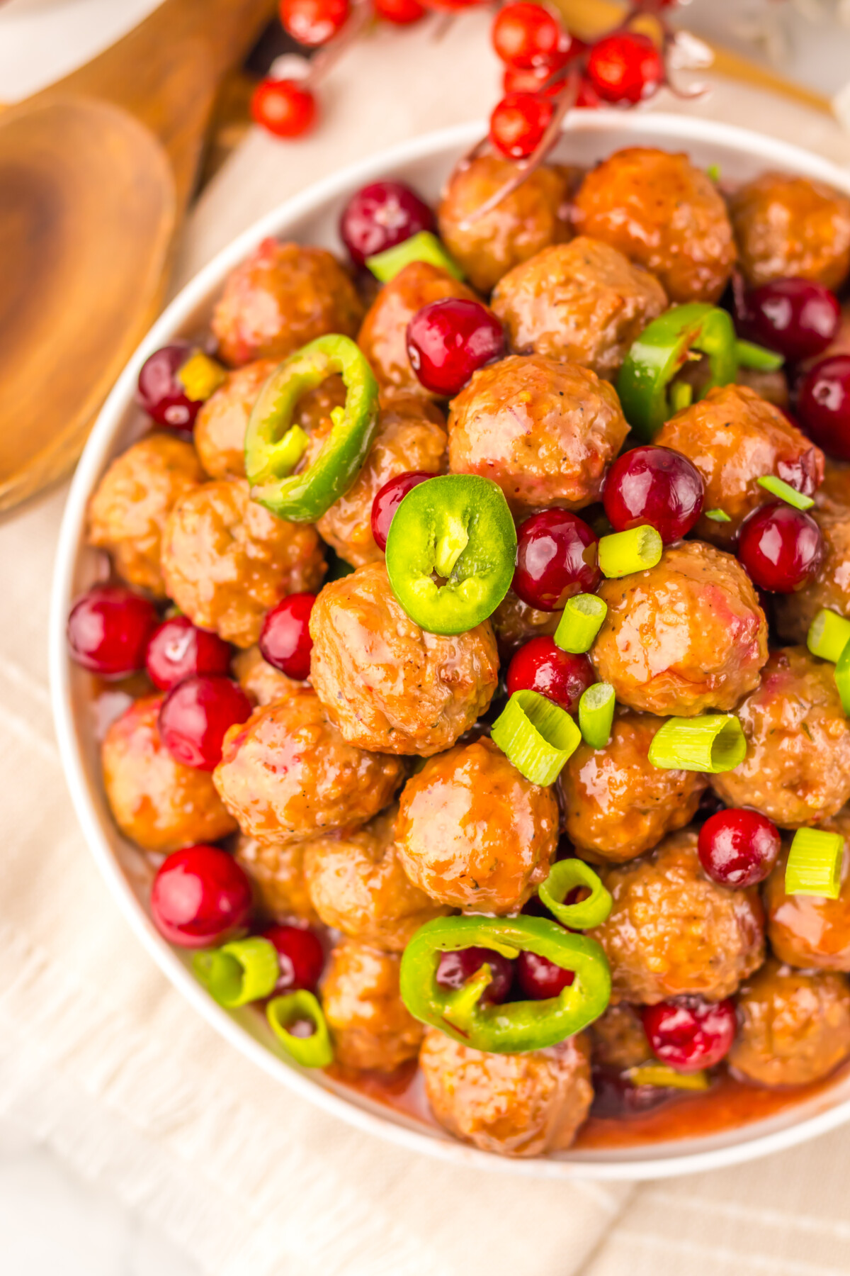 Slow cooker cranberry jalapeño meatballs in white bowl with glossy sauce, garnished with fresh cranberries and sliced jalapeños