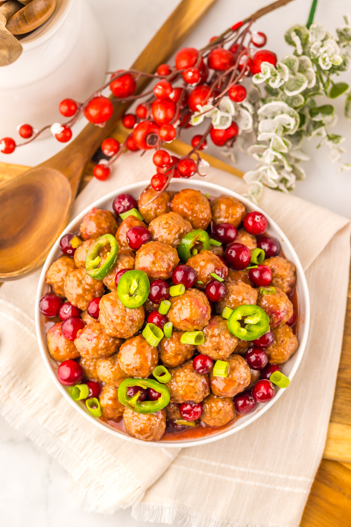 Slow cooker cranberry jalapeño meatballs in white bowl with jalapeño slices and fresh cranberries garnish