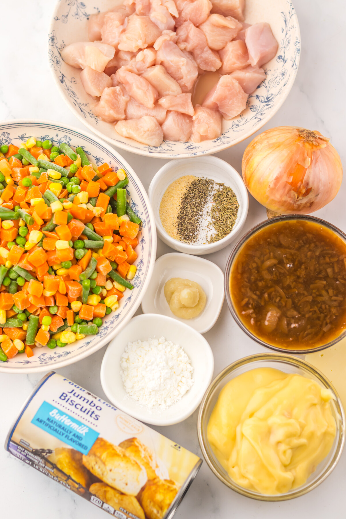 Slow cooker French onion chicken pot pie ingredients laid out including raw chicken, mixed vegetables, onion, seasonings, gravy, mayo and biscuits