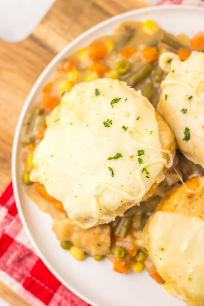 Slow cooker French onion chicken pot pie with cheese-topped biscuits and vegetables on white plate