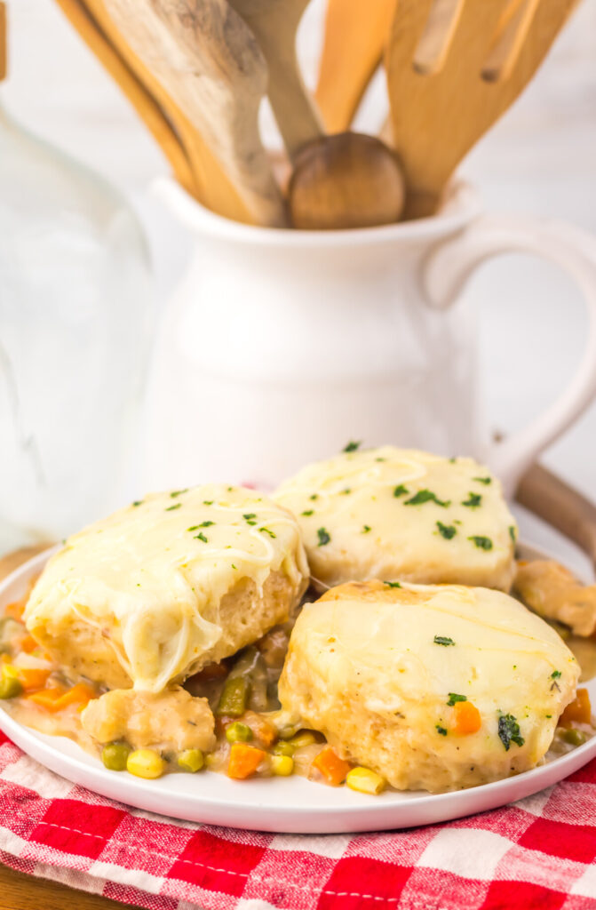 Slow cooker chicken pot pie with golden biscuit topping, corn and peas filling, garnished with parsley on white plate