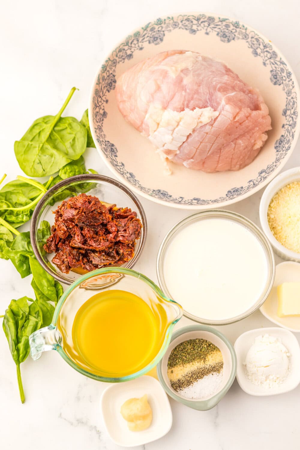 Slow cooker turkey breast ingredients laid out overhead including raw turkey breast, fresh spinach, sun-dried tomatoes, cream, and seasonings