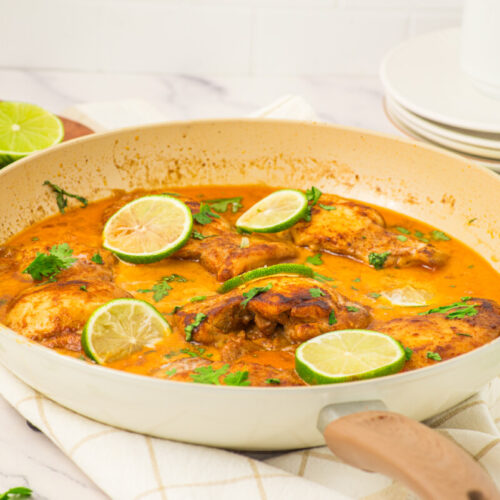 Coconut lime chicken curry in white skillet garnished with lime slices and cilantro