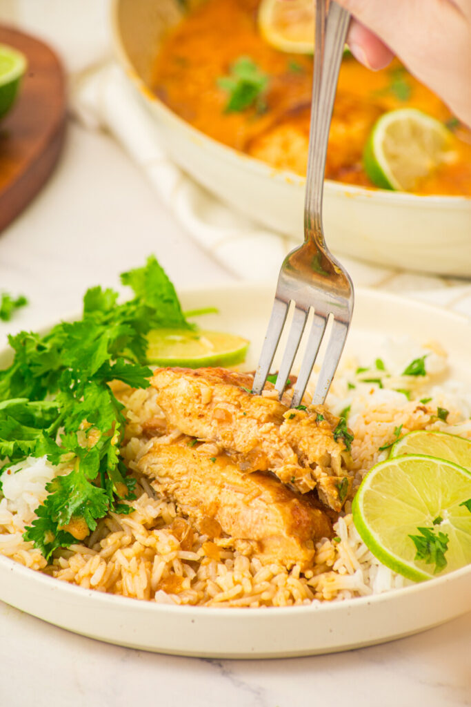 Coconut lime chicken served over rice with cilantro and lime garnish on a white plate