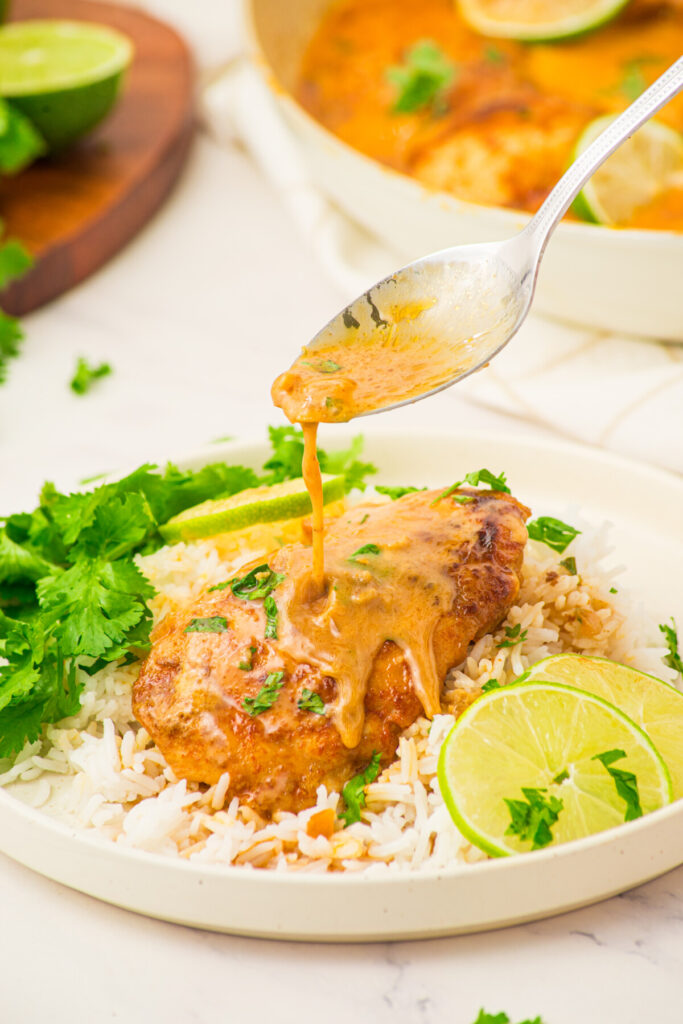 Coconut lime chicken with golden sauce drizzled over plated chicken breast, rice, and fresh cilantro garnish with lime wedges