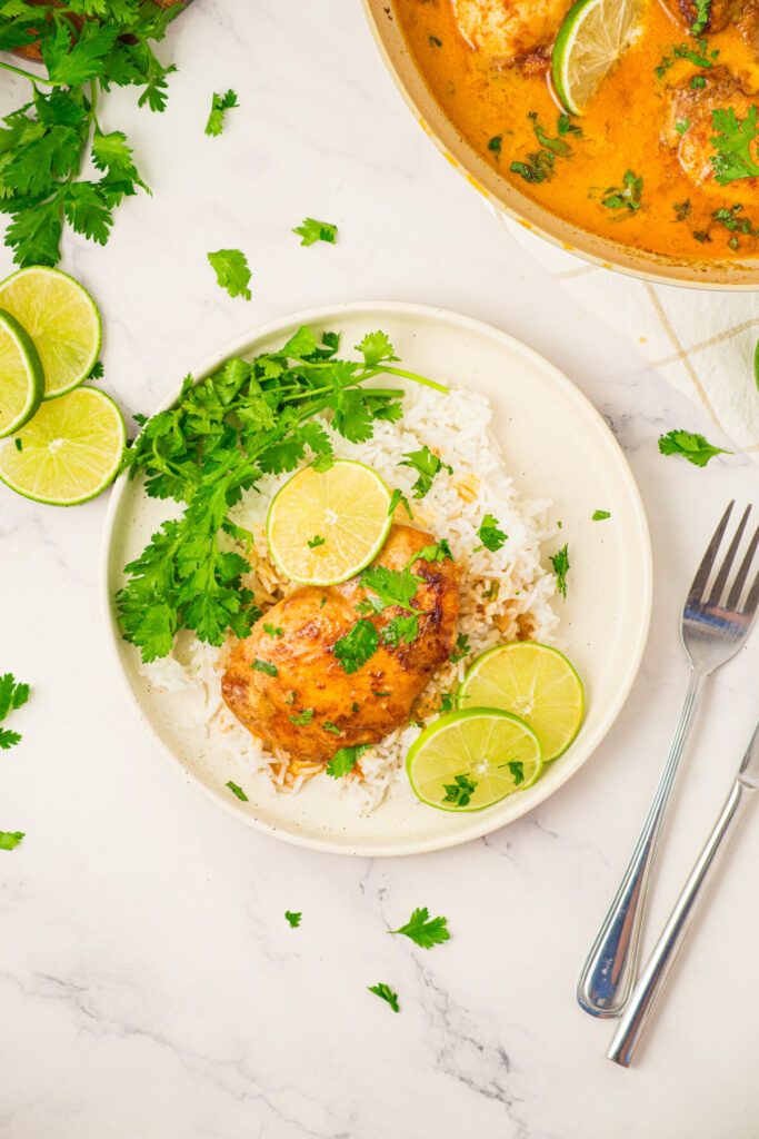 Coconut lime chicken served over white rice with cilantro garnish and lime slices on white plate