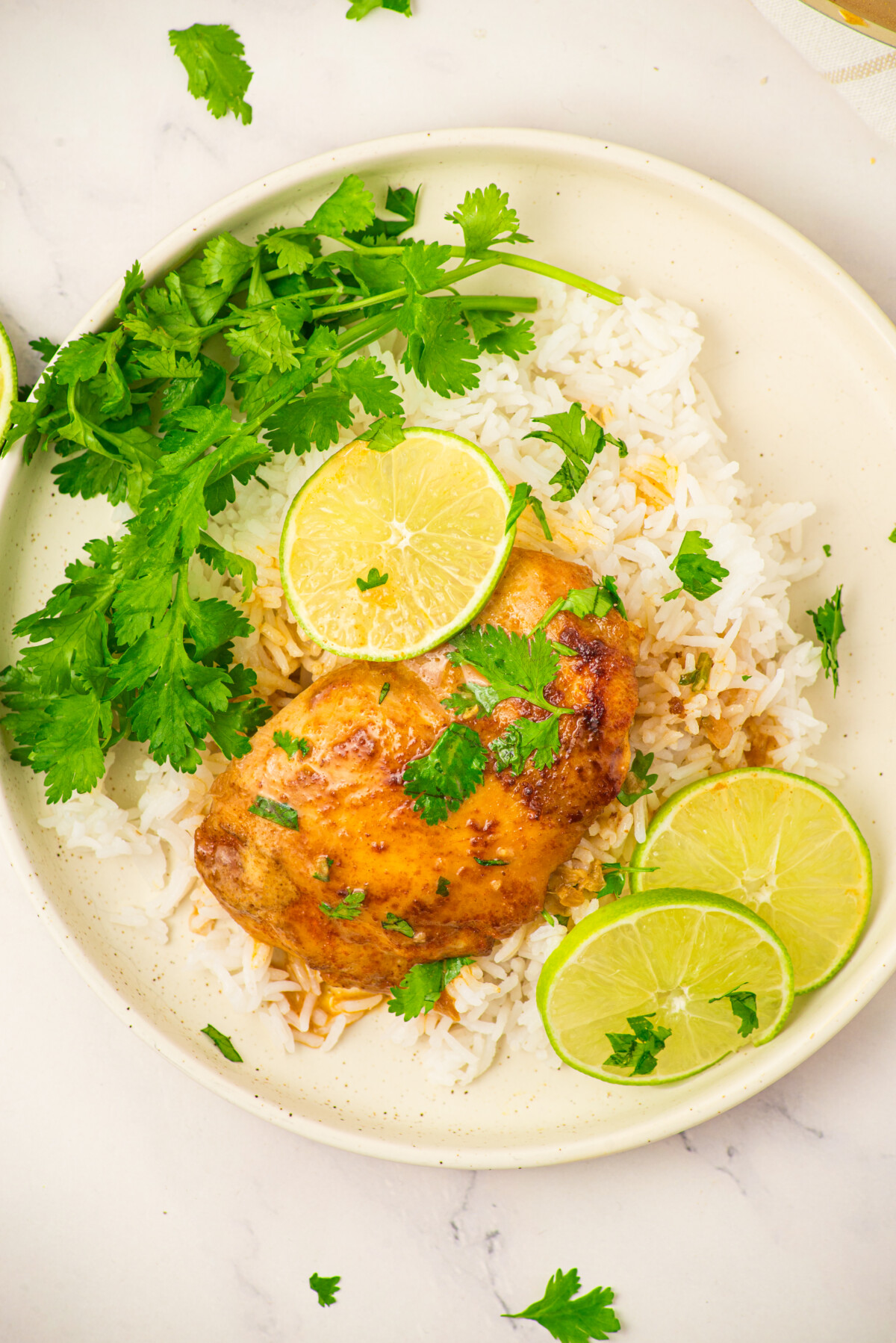 Coconut lime chicken breast with white rice, cilantro, and lime slices on a cream plate